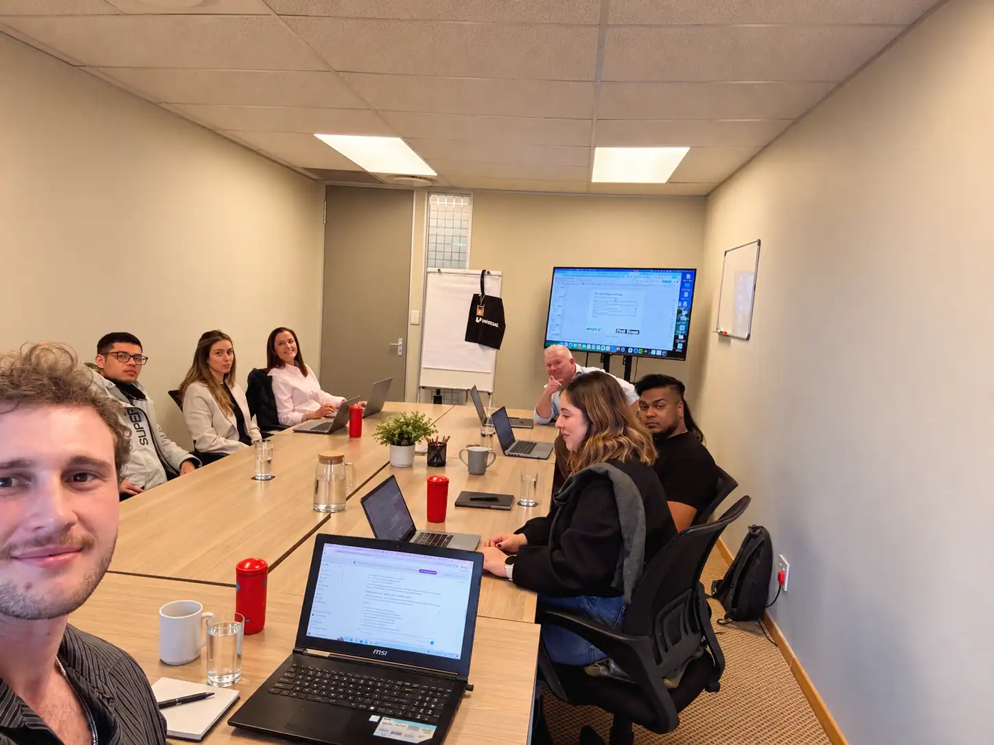 Business meeting with diverse team in a conference room with laptops and a large screen.